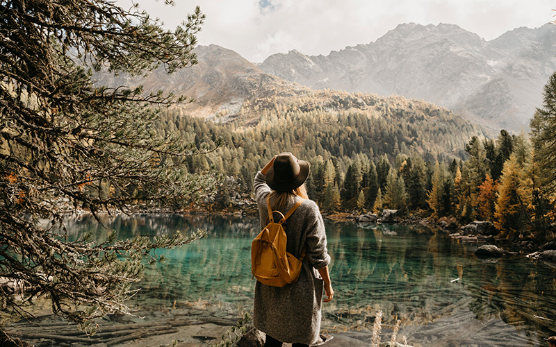 Donna con zaino e cappello ammira un lago nella foresta