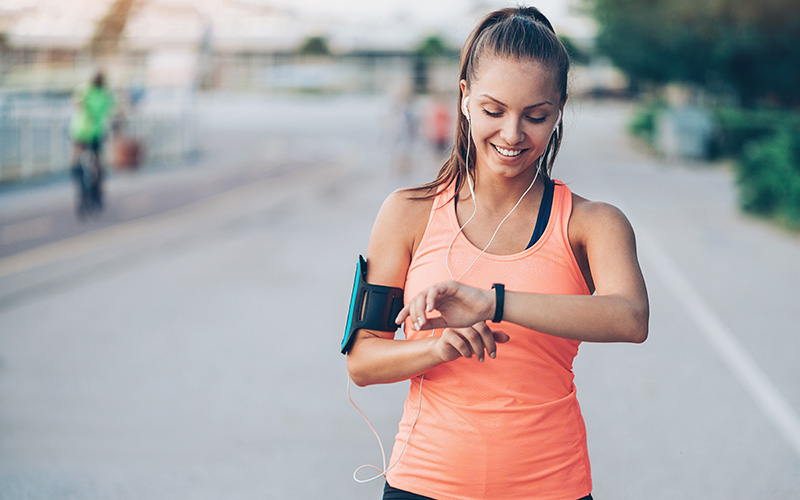 A white woman checks her fitness watch in the middle of exercise outdoors.