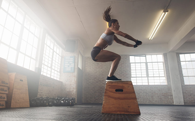 A white woman with long brown ponytail swinging above her head practices box jumps in hopes of achieving the afterburn effect