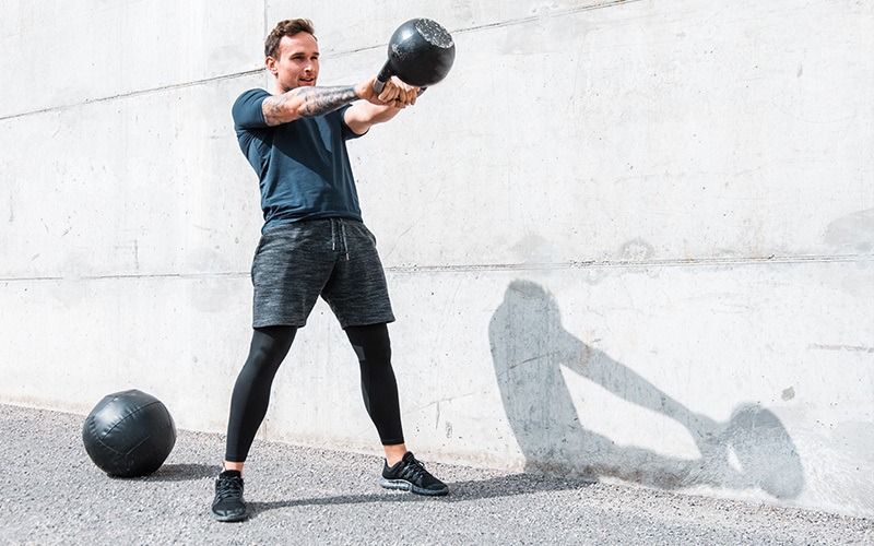 a white man swings a kettlebell during for body conditioning training