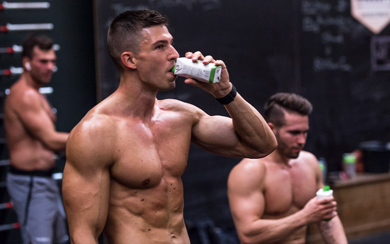 zwei sportliche Männer trinken Oberkörperfrei ein Kokoswasser von foodspring