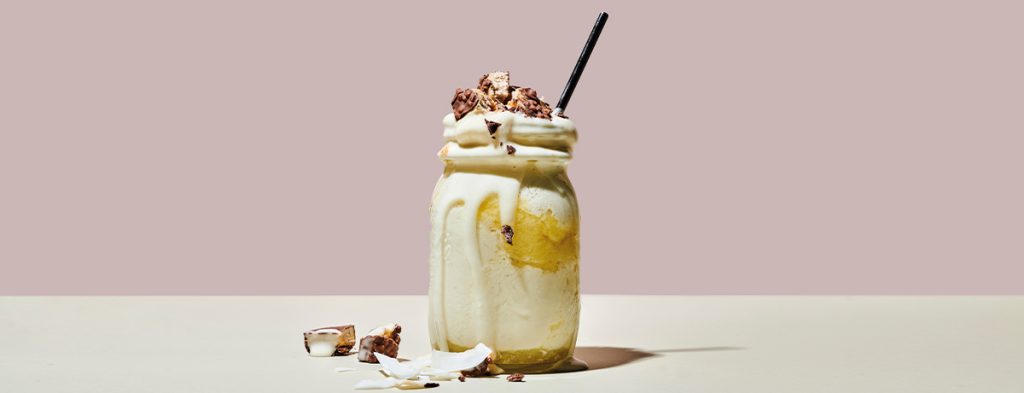 a layered pina colada protein shake in a Mason jar with a straw sticking out