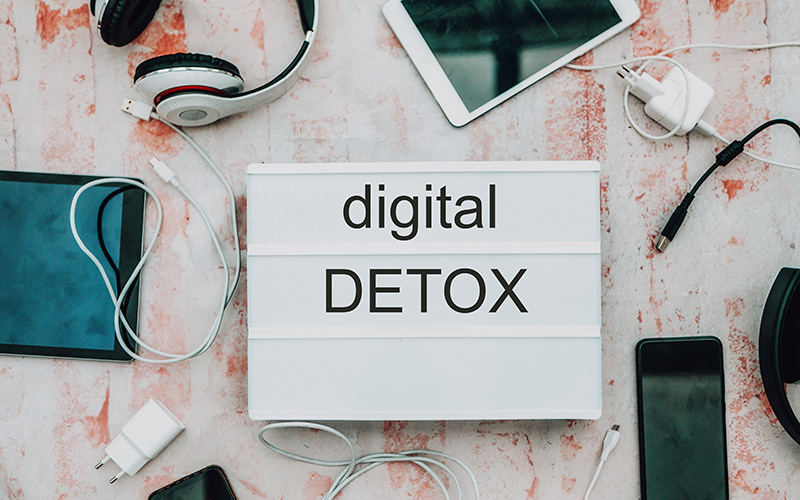 Leichtschild mit der Aufschrift digital Detox, daneben liegen Smartphones und Tablets