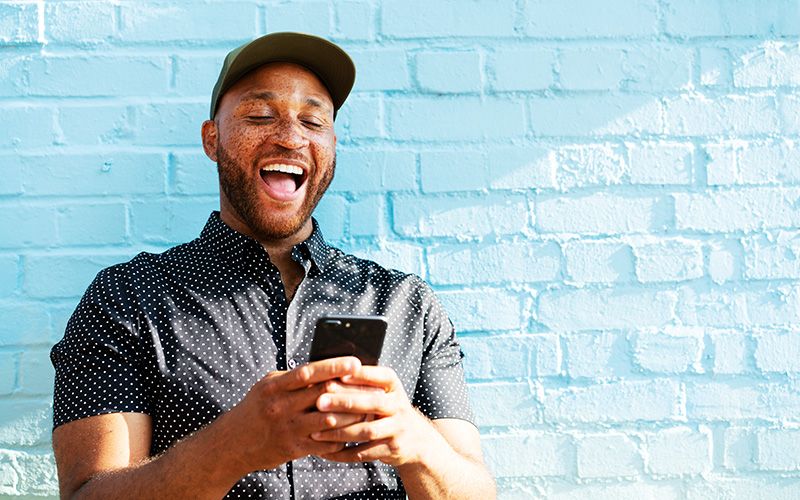 Ein Mann schaut glücklich und lachend auf sein Handy