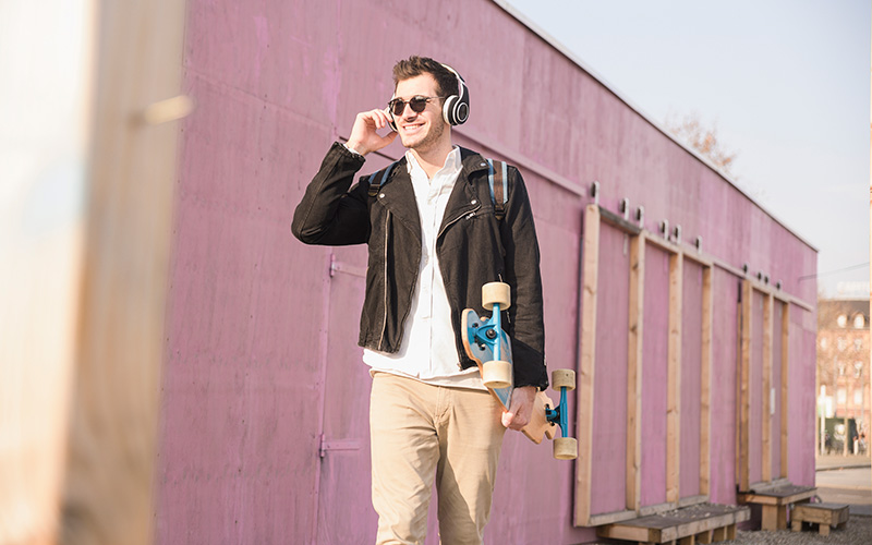 Mann läuft mit Kopfhörern und Skateboard duch die Stadt