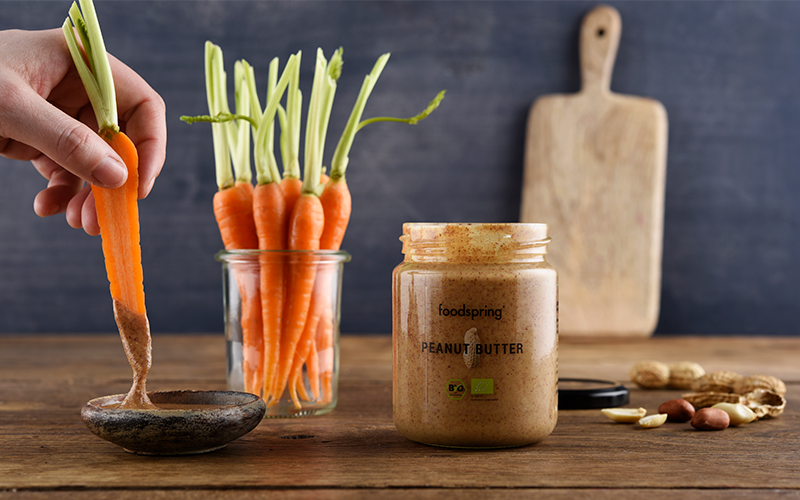 A carrot dips into peanut butter, begging the question: how healthy are peanuts?