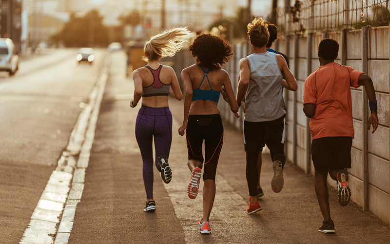 Eine Gruppe von jungen Leuten bei Joggen auf der Straße. Fotografiert von hinten
