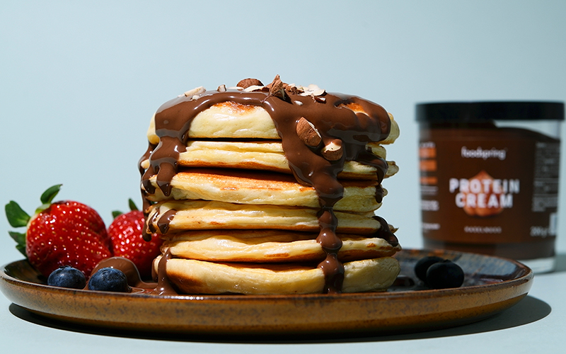 a stack of Protein Pancakes drizzled with rich brown Protein Cream and berries