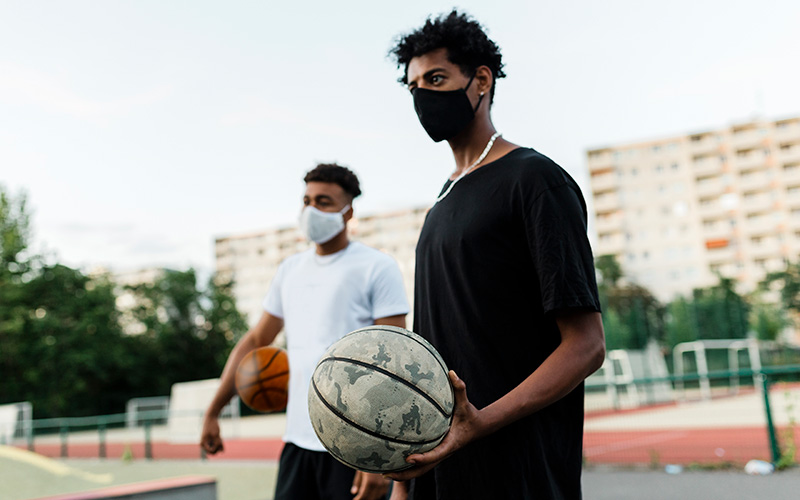 zwei junger Männer mit Maske auf dem Basketballplatz