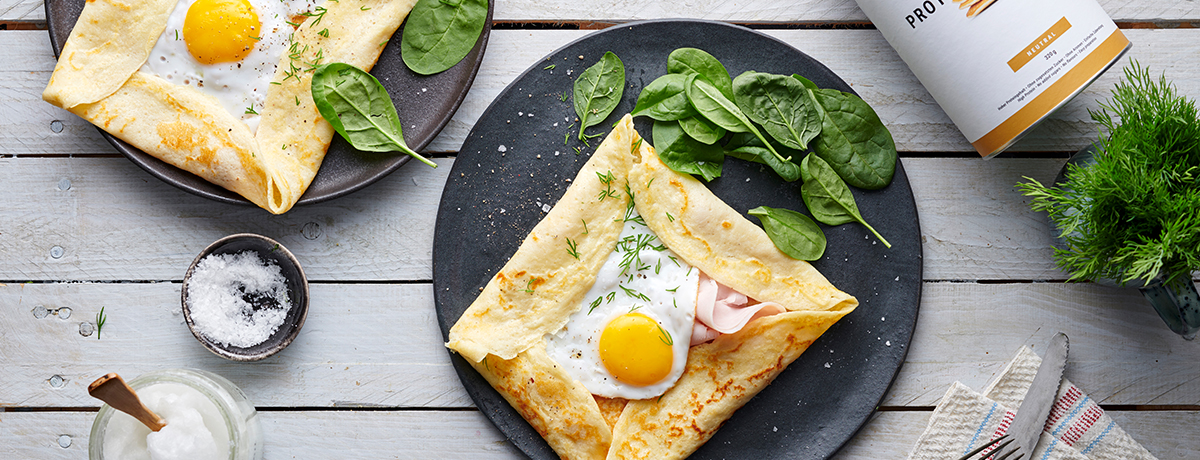 A plate of savory crepes with fried egg, with a few baby spinach leaves on the side for garnish