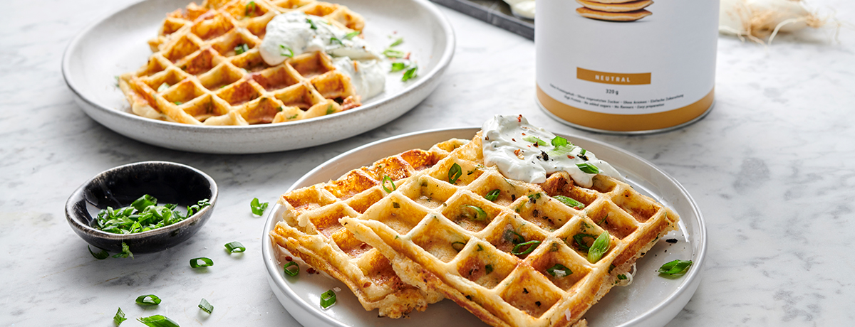A stack of two savory waffles garnished with chives and a dollop of sour cream