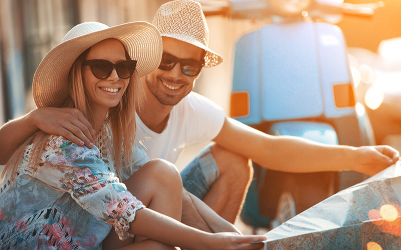 A man wraps his arm around a woman. Both are wearing straw hats and sunglasses and smiling. They are participating in a digital detox