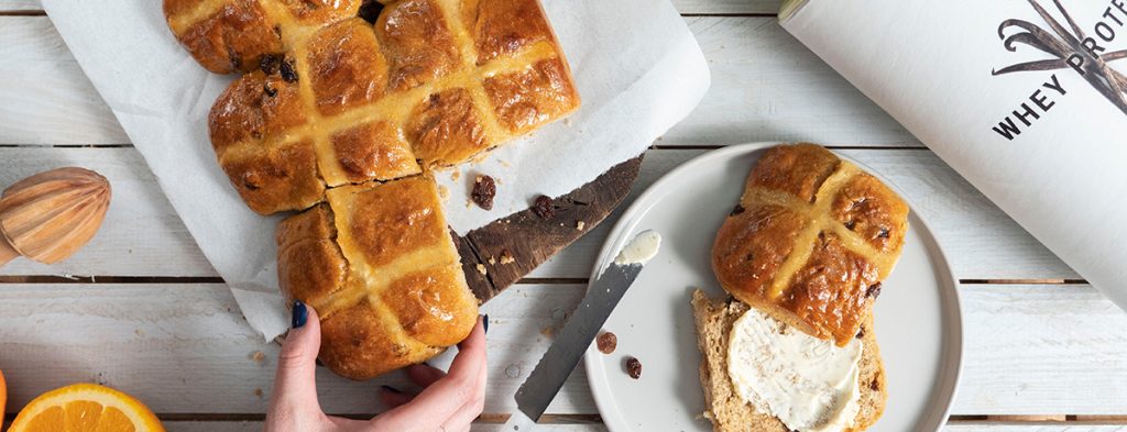 A light-skinned hand reaches for hot cross buns on a plate