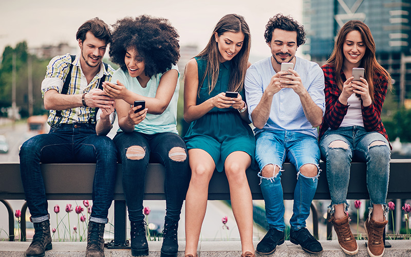 A group of mixed-race and -gender people look at each other's or their own phones with interested expressions