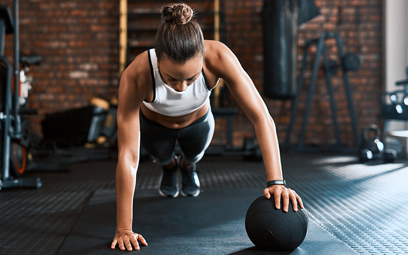 Eine Frau macht einen Liegestütz mit einer Hand auf einem Ball.
