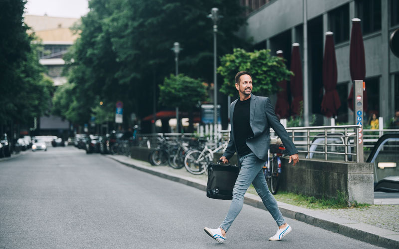 Mann im Business Outfit und Sportschuhen rennt über eine Straße