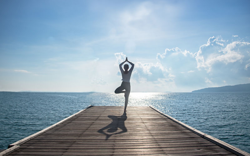 Frau macht auf einem Steg eine einbeinige Yogapose