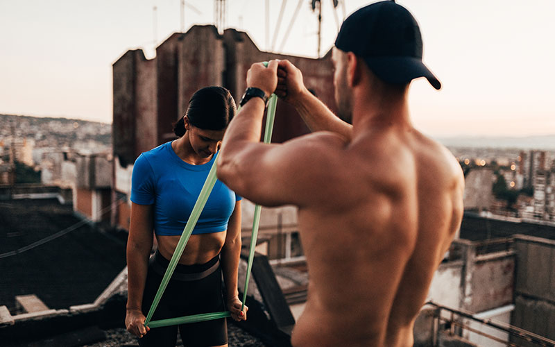 Mann und Frau trainieren auf dem Dach mit Fitnessbändern