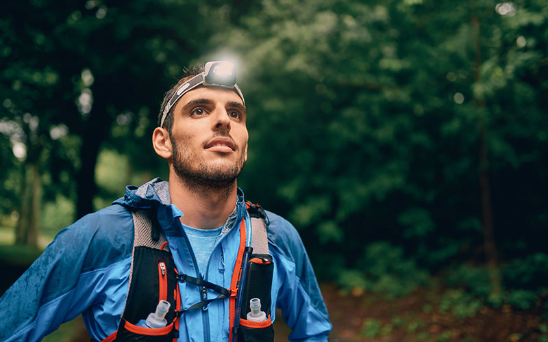 Trailrunner mit Rucksack und Stirnlampe im Wald