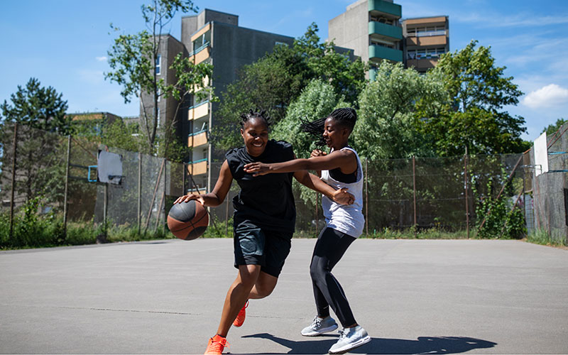 Due ragazze giocano a basket in un campetto all'aperto
