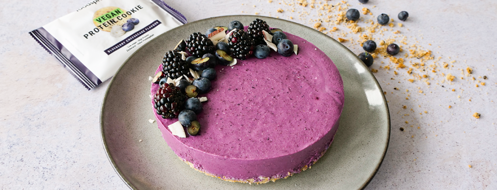 a bright purple blueberry cheesecake garnished with a decorative edge of blueberries, blackberries, and coconut chips
