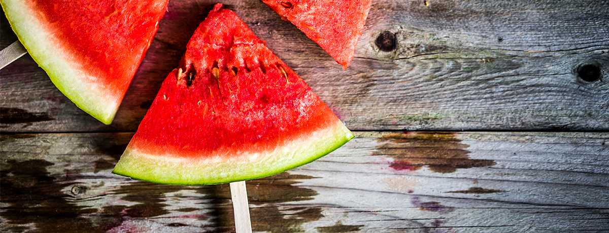 A frozen triangle of watermelon with a popsicle stick poking out from the rind