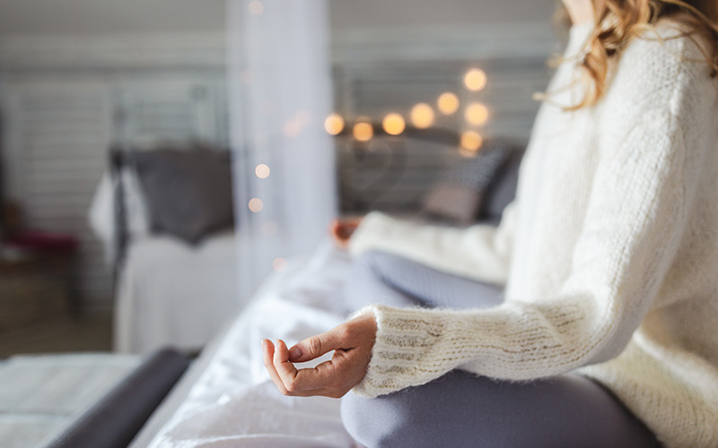 A white woman's arms, torso and folded legs take up the right-hand third of the photo frame as she meditates for a healthy december
