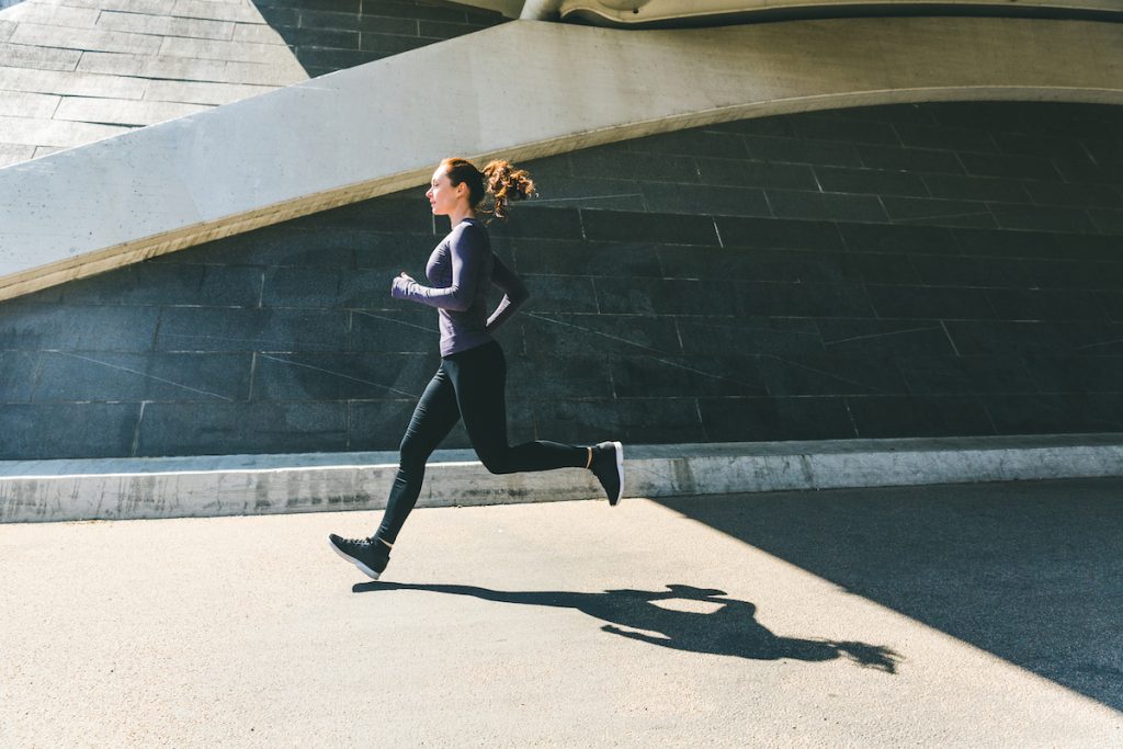 Woman jogging or running, side view with her shadow on the ground. Girl wearing sportswear doing fitness activities outdoors. Healthy lifestyle and sport concepts