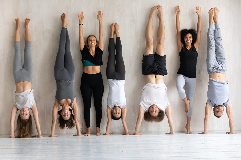 A group of seven white people in front of a wall. Five are doing a handstand, and two are not. The four are trying to change your mindset.