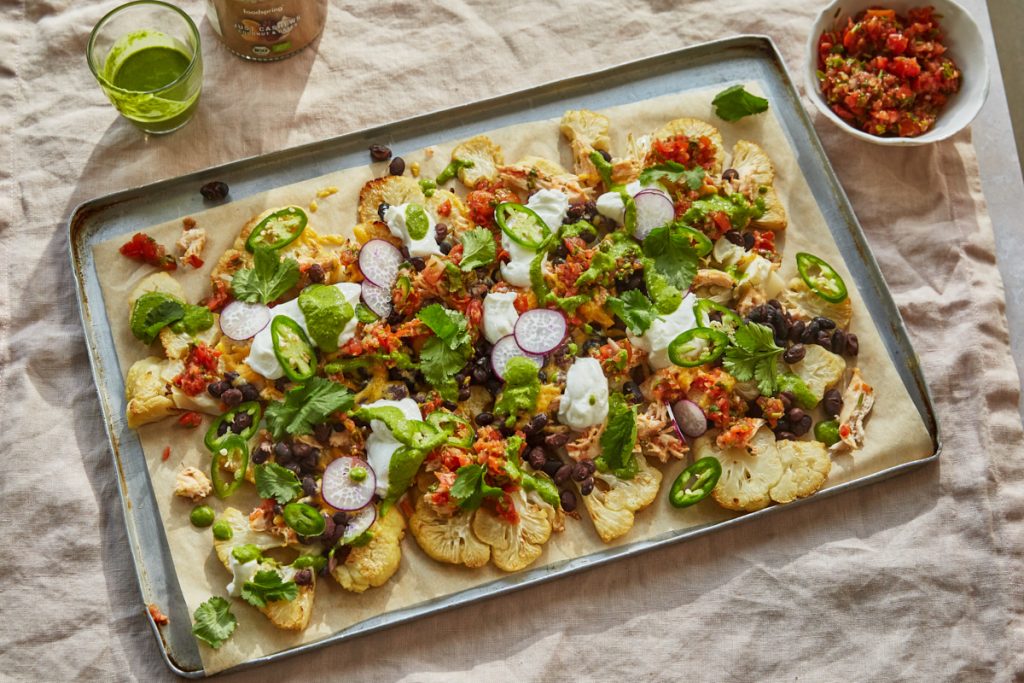 a tray with cauliflower nachos, a bowl of tomato salsa and a glass of coriander dressing