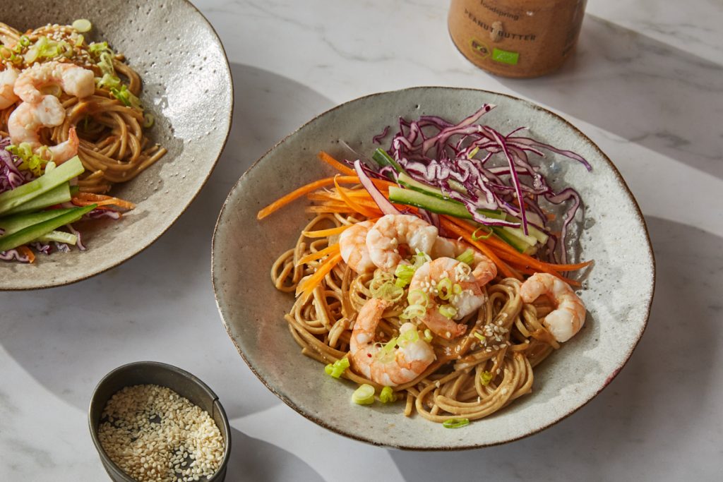 two bowls of sesame noodles topped with shredded vegetables and prawns
