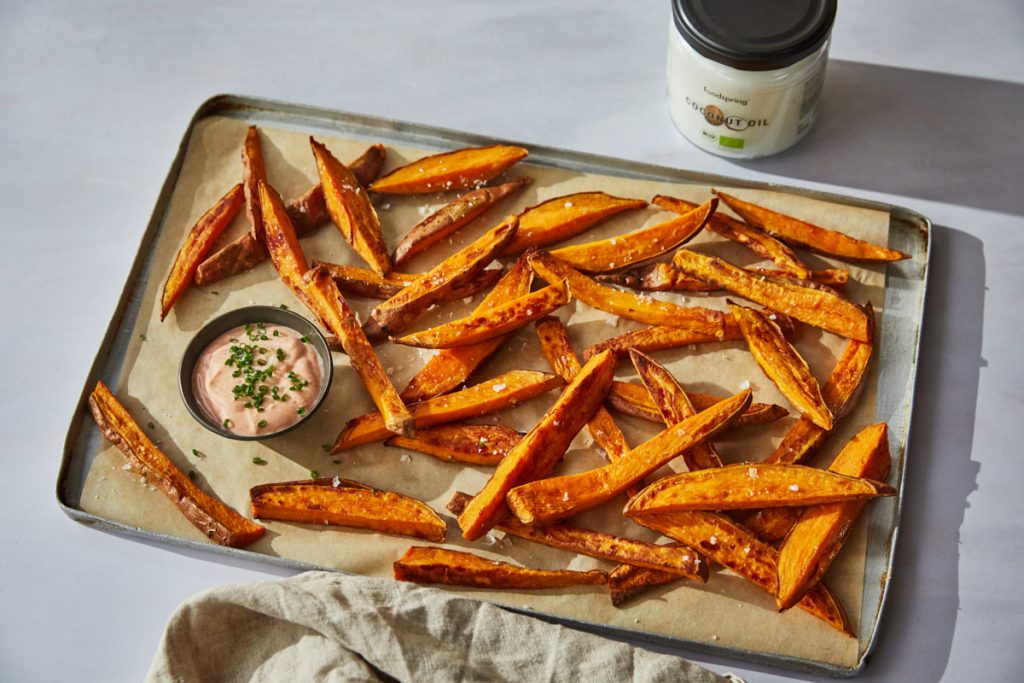 sweet potato fries on a baking tray with a pot of creamy protein dip