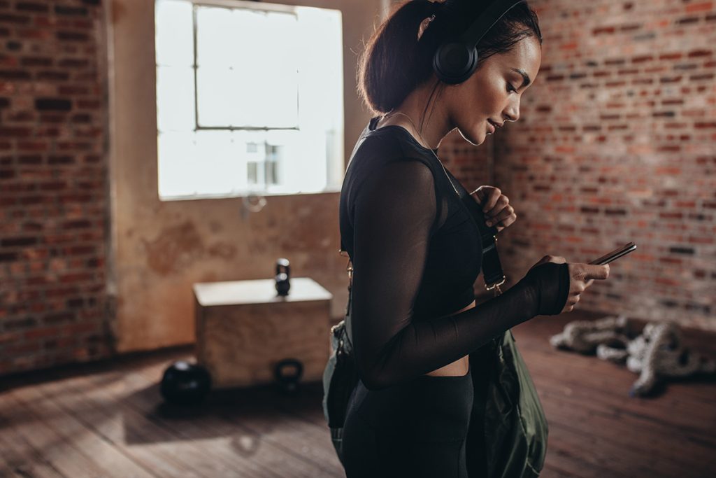 A woman of color checks her phone before making sure her workout bag has all the gym bag essentials she'll need