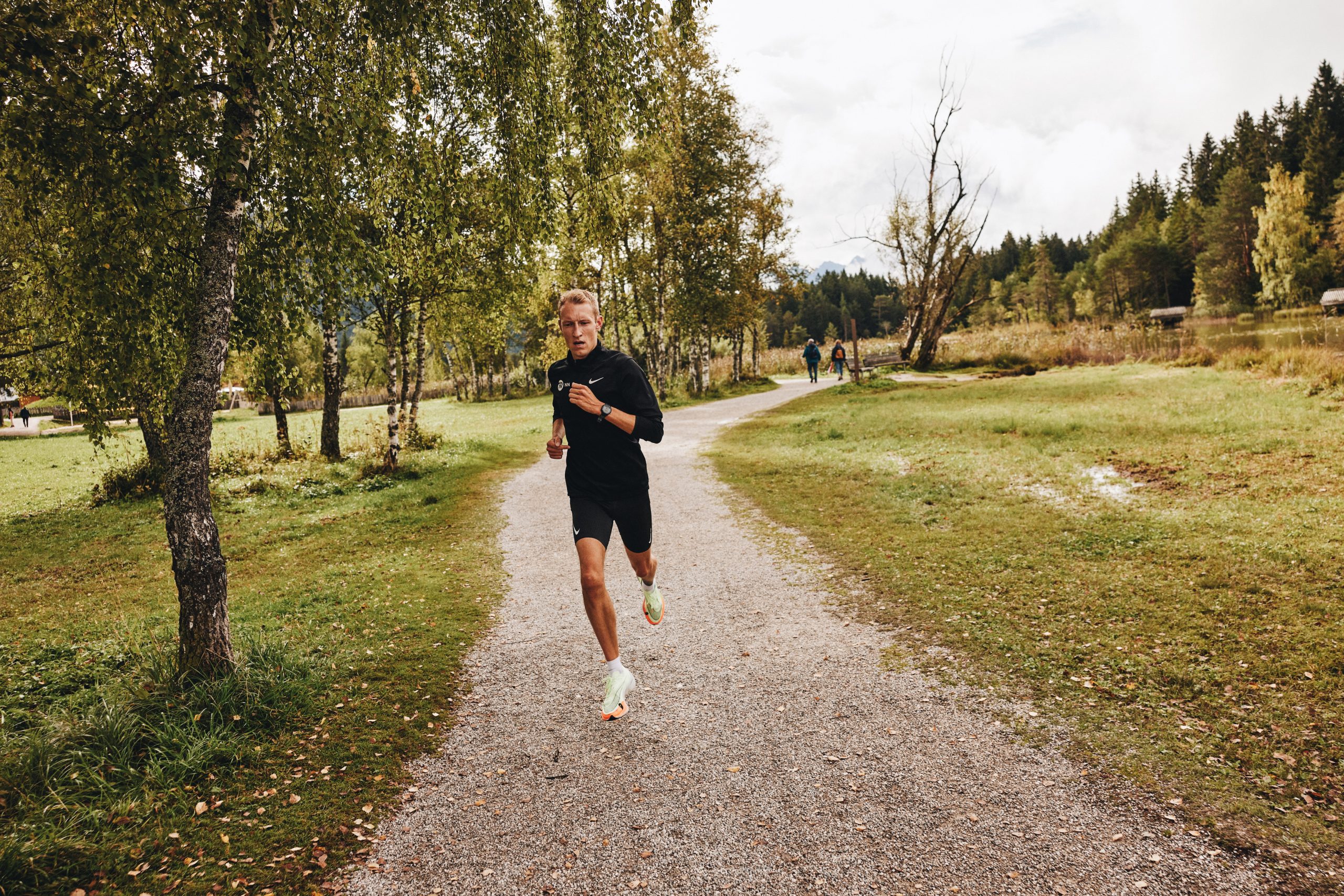 Björn Koreman runs on a gravel trail through the woods wearing shorts and a long-sleeve top.